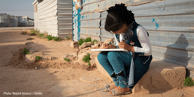 A young girl sits, writing in a pad.