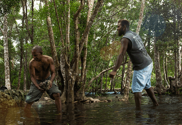Two men shift buckets of water from a flooded stream.