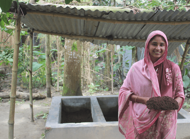 A young woman in a pink sari stands in front of her thriving garden.