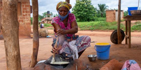 A young woman sits near a cooking pot.