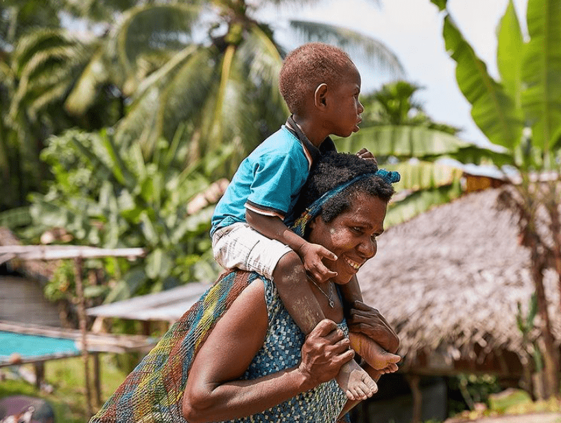 A mother carries her young child on her shoulder.