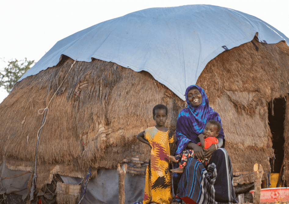 A woman sits with her children outside their home
