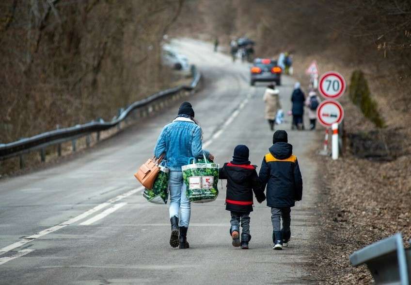 A mother and her two children walk away from the camera down a long road.