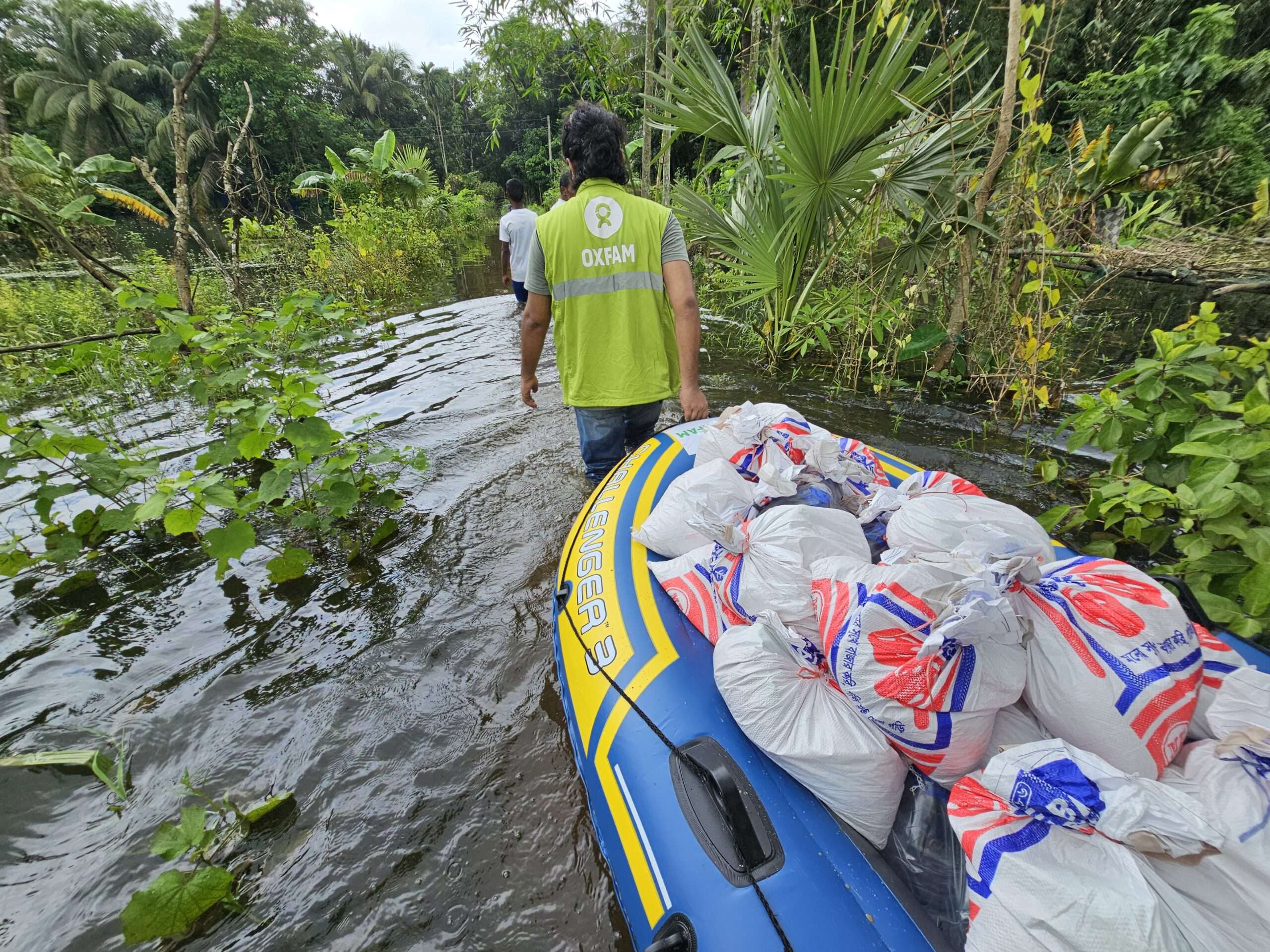 Oxfam staff carrying supplies through floodwaters