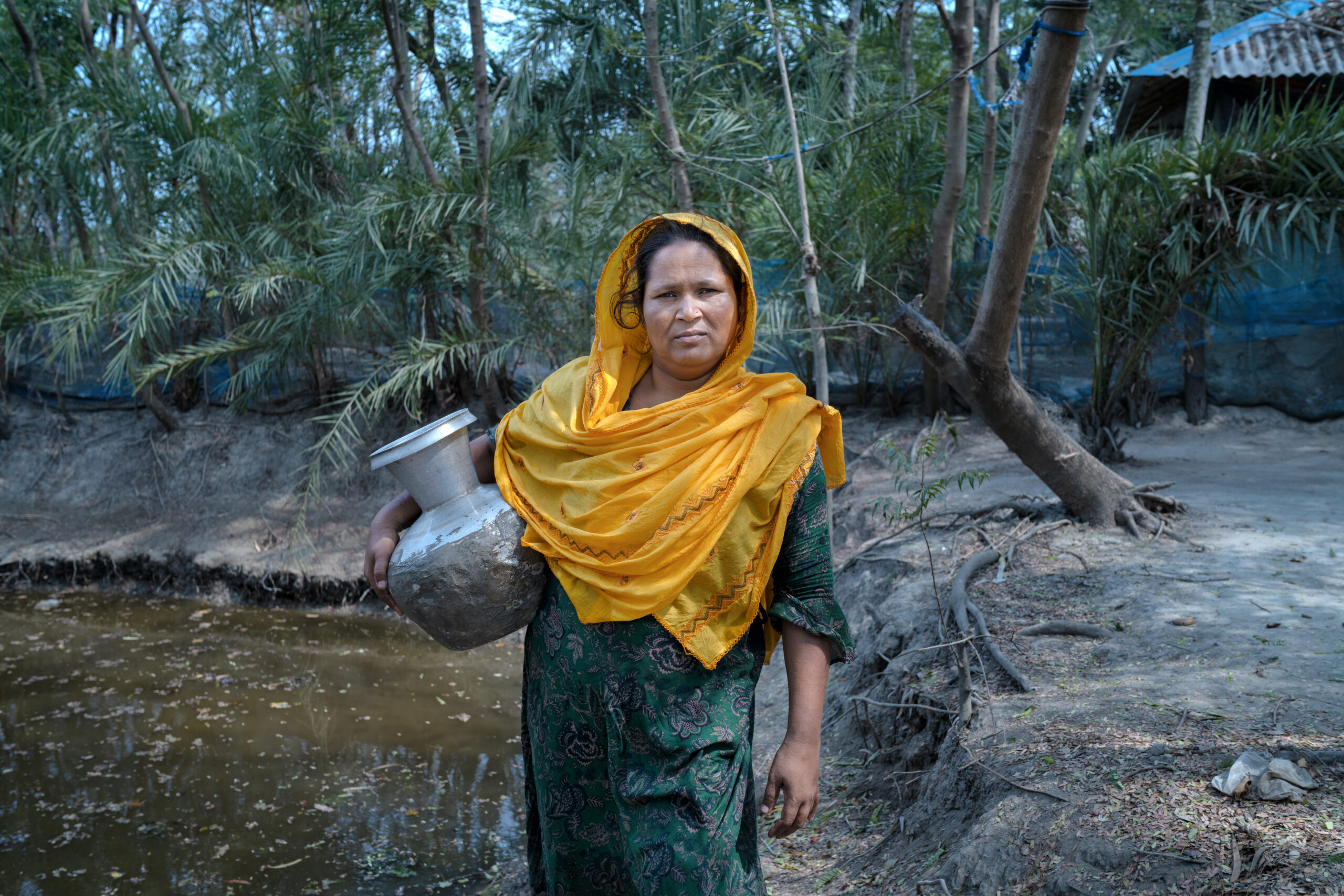 Woman holding water vase in front of a lake in Bangladesh