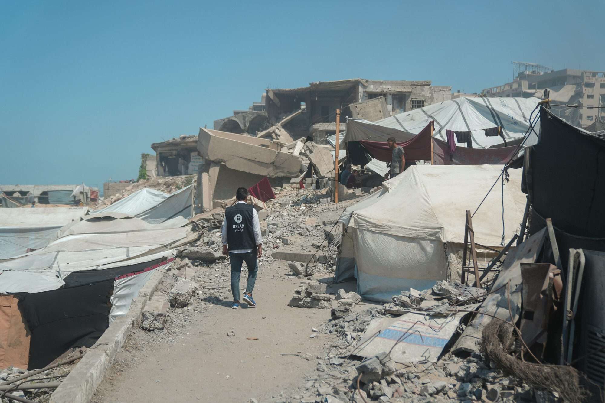 Osama, Oxfam Staff, walks among tents and rubble in Gaza City - photo credit Alef Multimedia / Oxfam