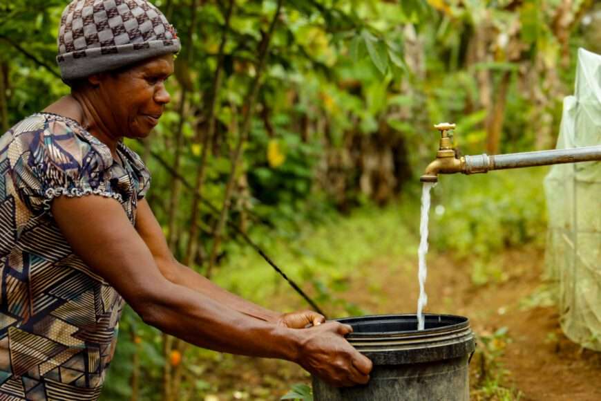 Papua New Guinean woman filling bucket with clean water