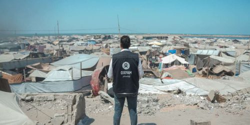 Osama, Oxfam Staff, walks among tents and rubble in Gaza City
